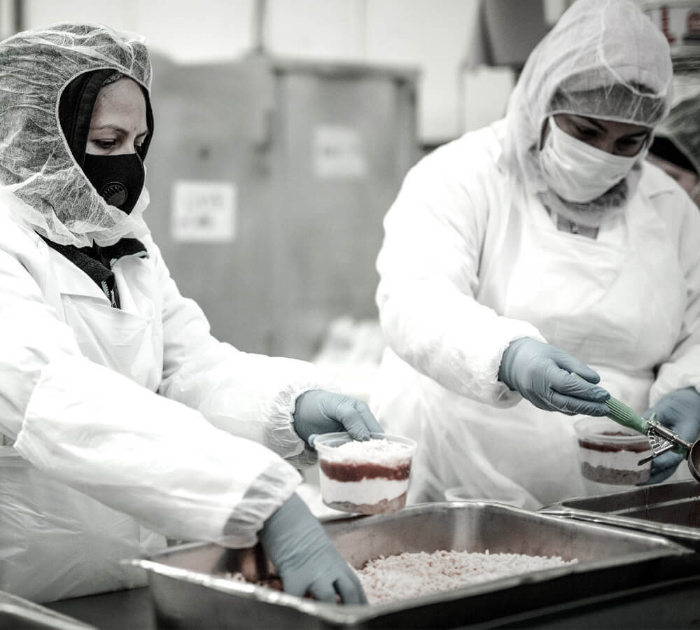 Brett Anthony Foods' Full-Service Prepared Foods Solution, with two commercial kitchen workers assembling prepared foods products.